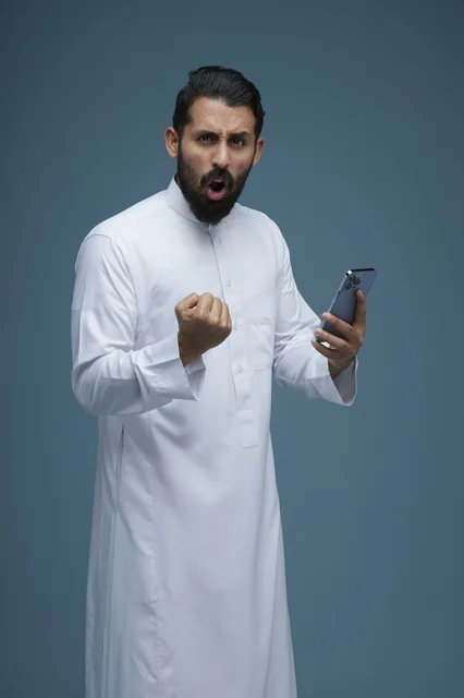 رجل سعودي بالثوب التقليدي يعبر عن فرحته باستخدام الجوال