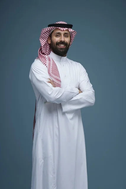 رجل سعودي بالزي التقليدي يبتسم أمام خلفية زرقاء