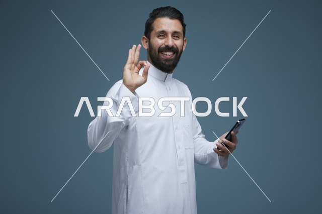 رجل سعودي يحمل هاتف ذكي مع إيماءة موافقة