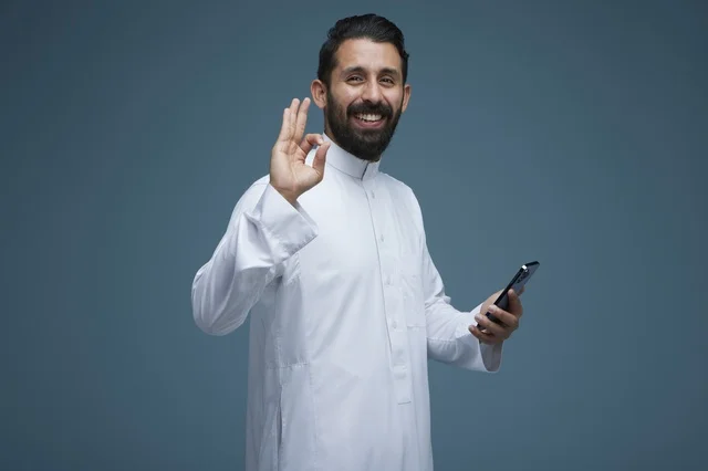 رجل سعودي يحمل هاتف ذكي مع إيماءة موافقة