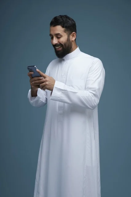 رجل سعودي بالثوب التقليدي يستخدم الهاتف الذكي
