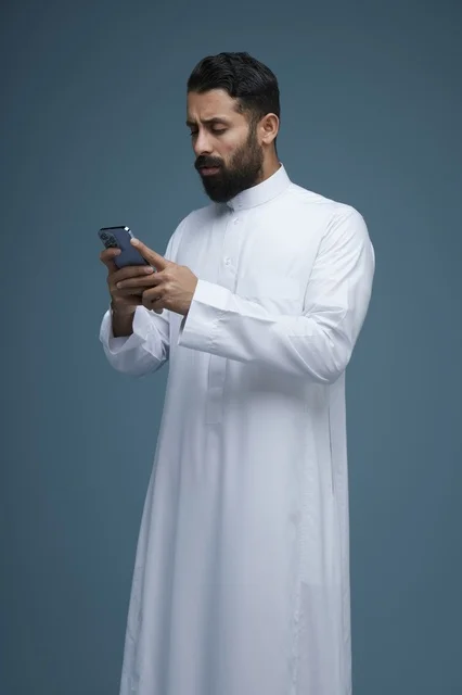 رجل سعودي بالثوب التقليدي يستخدم الهاتف الذكي في استوديو