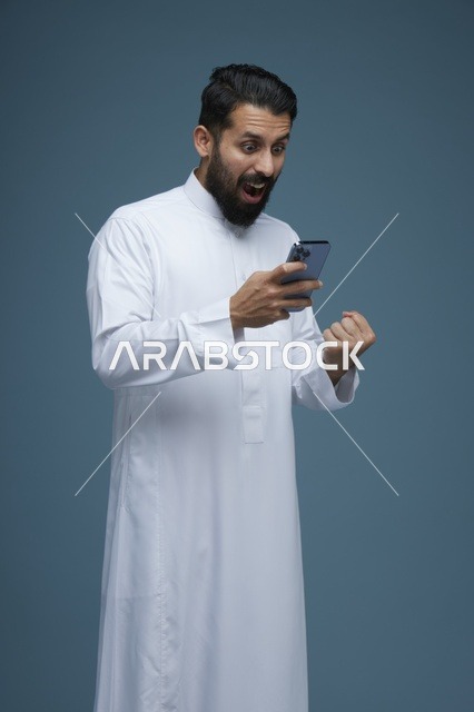 رجل سعودي متحمس يستخدم الهاتف الذكي بالثوب التقليدي
