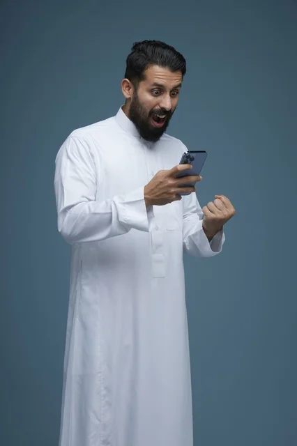 رجل سعودي متحمس يستخدم الهاتف الذكي بالثوب التقليدي