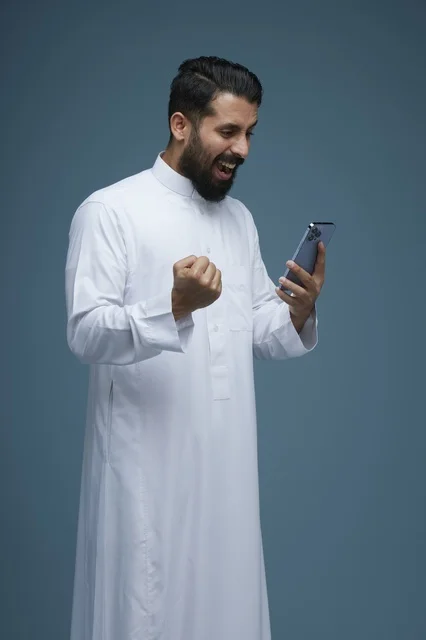 رجل سعودي بالثوب التقليدي يحتفل بنجاح عبر الهاتف الذكي