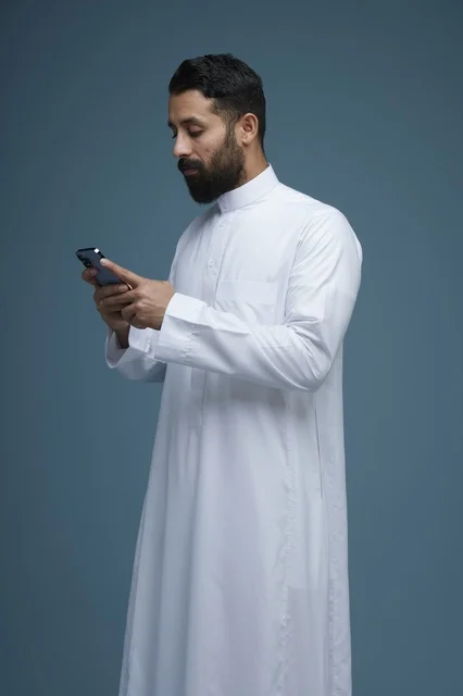 رجل سعودي بالثوب التقليدي يستخدم الهاتف الذكي