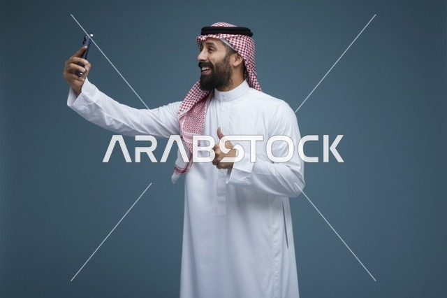 رجل سعودي يلتقط سيلفي بالهاتف الذكي مع إيماءة الإبهام