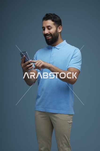 رجل سعودي يستخدم الهاتف الذكي بملابس كاجوال في الاستوديو