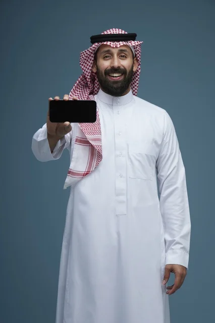 رجل سعودي يبتسم ويمسك هاتف ذكي بالثوب والشماغ