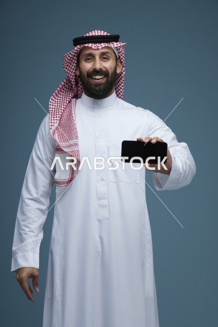 رجل سعودي مبتسم يحمل هاتف ذكي بخلفية زرقاء