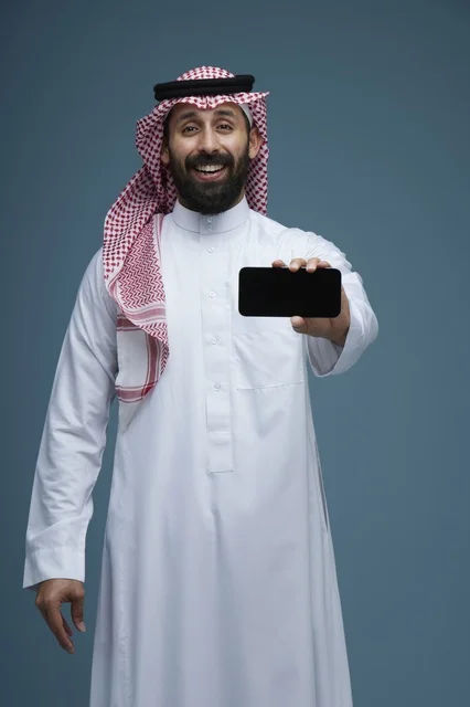 رجل سعودي يبتسم يحمل هاتف ذكي أمام خلفية زرقاء