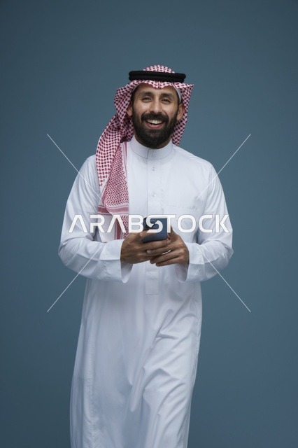 رجل سعودي مع هاتف ذكي بالثوب التقليدي في استوديو