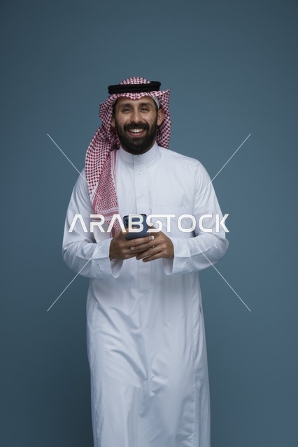 رجل سعودي مبتسم يحمل هاتف ذكي في الاستوديو
