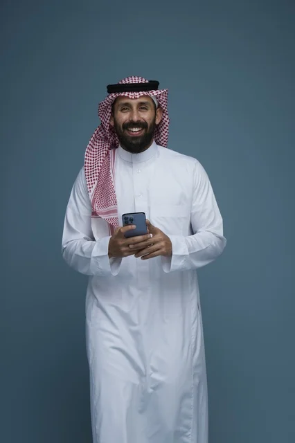 رجل سعودي مبتسم يحمل هاتف ذكي في الاستوديو