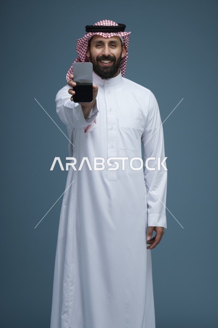 رجل سعودي يحمل هاتفاً ذكياً على خلفية زرقاء