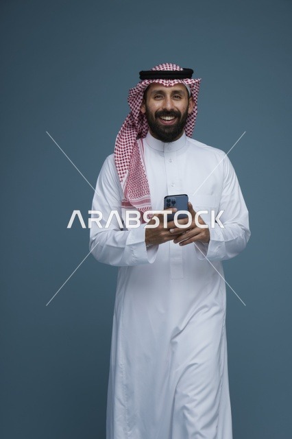 رجل سعودي يستخدم الهاتف الذكي بالزي التقليدي في الاستوديو