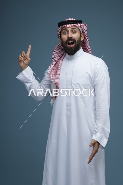 رجل سعودي يشير للأعلى بتعبير وجه متفاجئ في الاستوديو