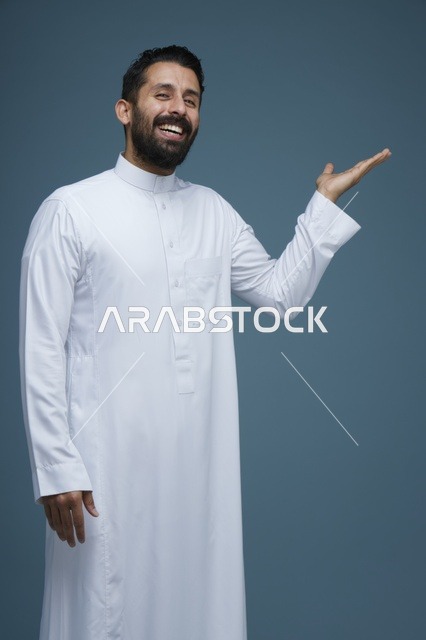 رجل سعودي بالثوب الأبيض يشير بيديه أمام خلفية زرقاء