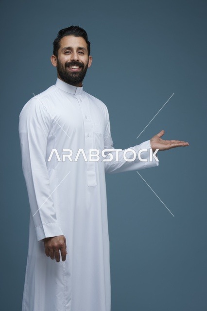 رجل سعودي بالثوب الأبيض يبتسم ويشير بيده