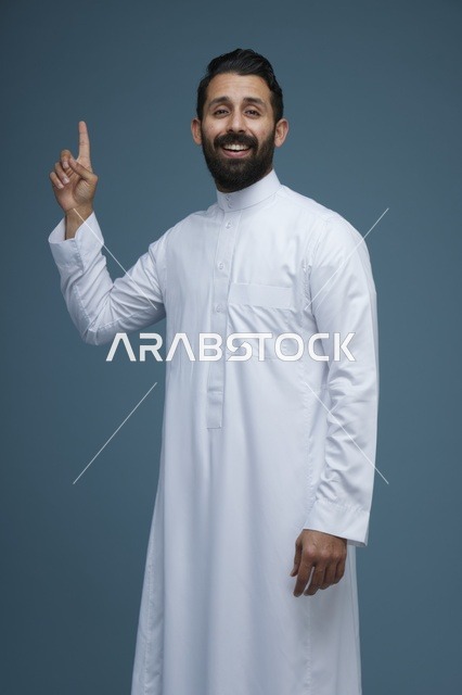 رجل سعودي يرتدي الثوب الأبيض يشير بإصبعه للأعلى مبتسماً