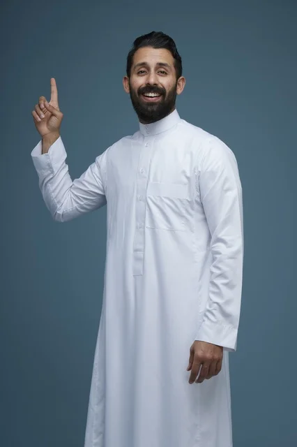 رجل سعودي يرتدي الثوب الأبيض يشير بإصبعه للأعلى مبتسماً