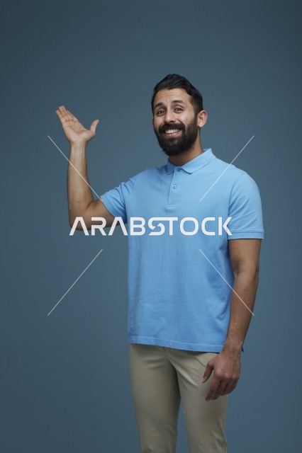 رجل سعودي يشير بيده بملابس كاجوال خلفية زرقاء