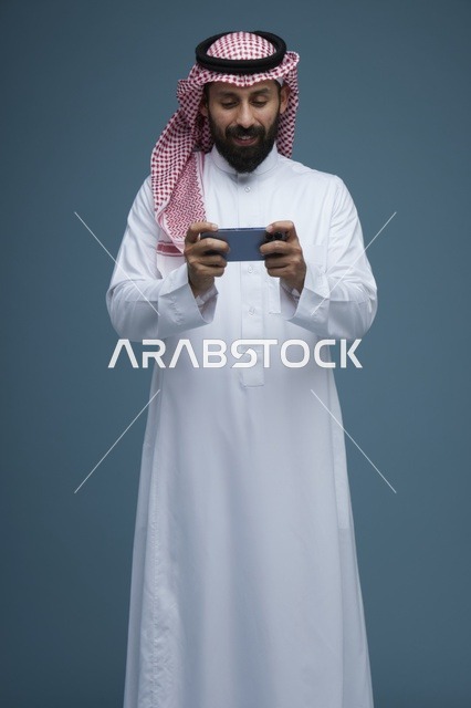 رجل سعودي يلعب بالهاتف الذكي في استوديو بخلفية زرقاء