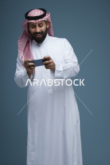 رجل سعودي يلعب بهاتف ذكي بالزي التقليدي