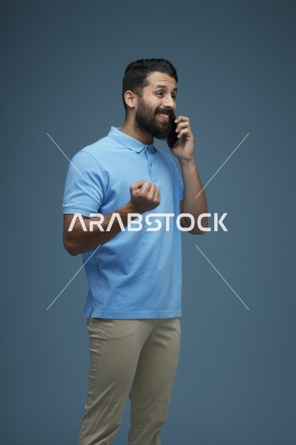 رجل سعودي يتحدث عبر الهاتف الذكي بملابس كاجوال خلفية زرقاء