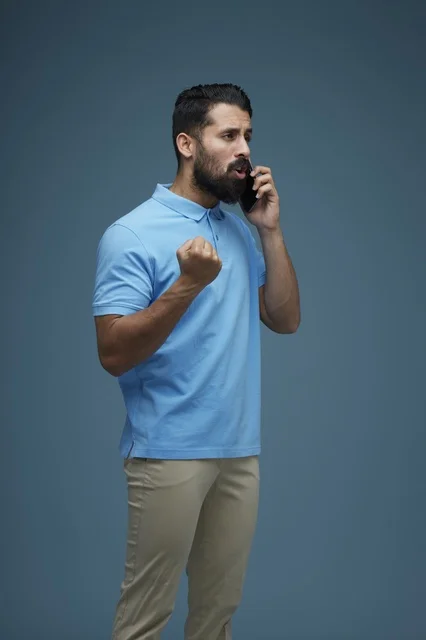 Saudi Man in Casual Attire Using Smartphone on Blue Background