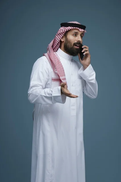 رجل سعودي بالزي التقليدي يتحدث عبر الهاتف الذكي