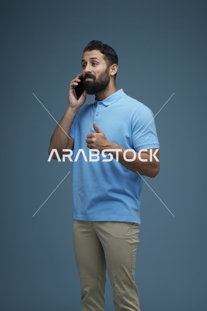 رجل سعودي يتحدث بالهاتف الذكي بخلفية استوديو زرقاء