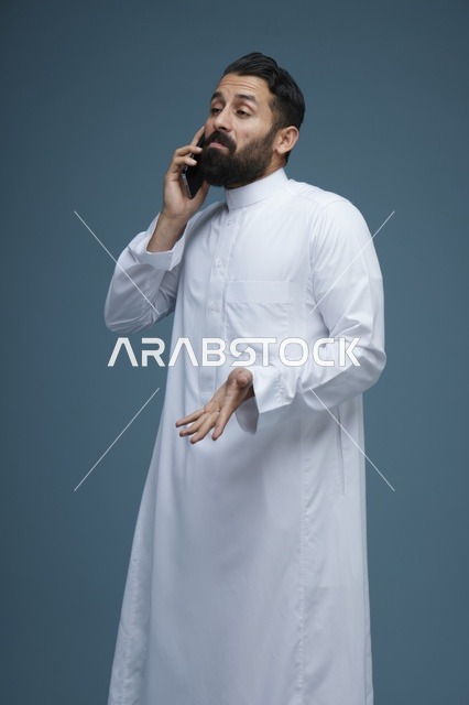 رجل سعودي بالثوب يتحدث عبر الهاتف الذكي في استوديو