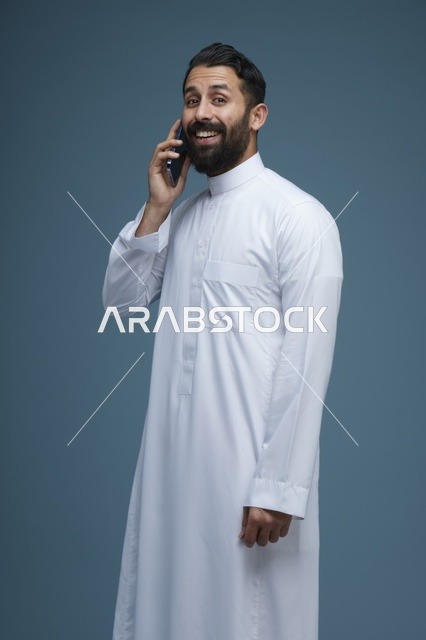 رجل سعودي مبتسم يتحدث بالجوال بالثوب التقليدي