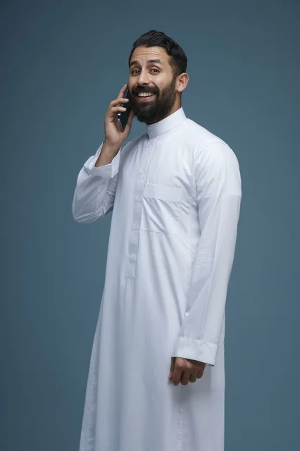 رجل سعودي مبتسم يتحدث بالجوال بالثوب التقليدي
