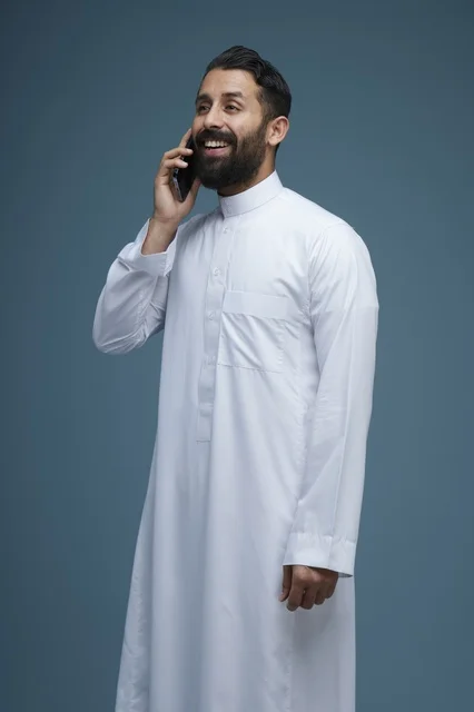 رجل سعودي مبتسم يتحدث عبر الهاتف الذكي بالثوب الأبيض
