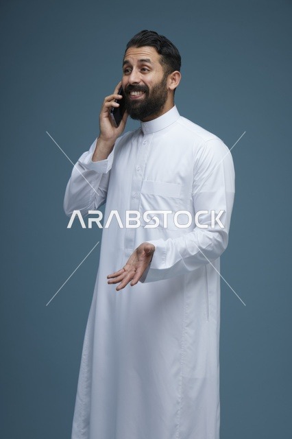 رجل سعودي مبتسم يرتدي الثوب يتحدث عبر الهاتف الذكي