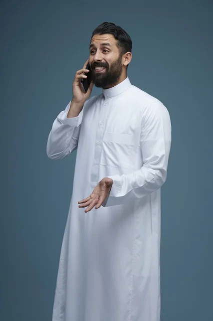 رجل سعودي مبتسم يرتدي الثوب يتحدث عبر الهاتف الذكي