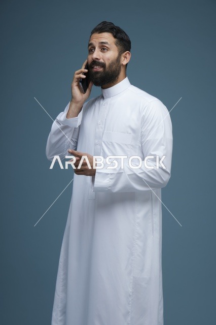 رجل سعودي بالثوب الأبيض يتحدث عبر الهاتف الذكي