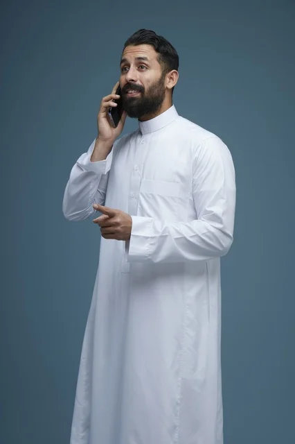 رجل سعودي بالثوب الأبيض يتحدث عبر الهاتف الذكي