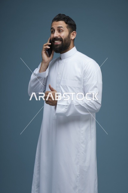 رجل سعودي مبتسم يتحدث عبر الهاتف الذكي في الاستوديو
