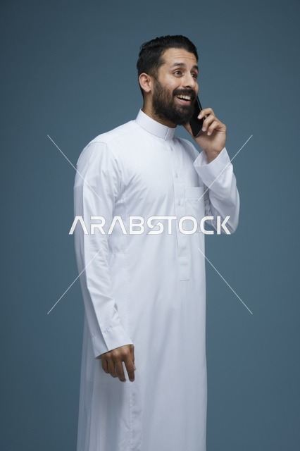 رجل سعودي مبتسم يتحدث عبر الهاتف الذكي بالثوب