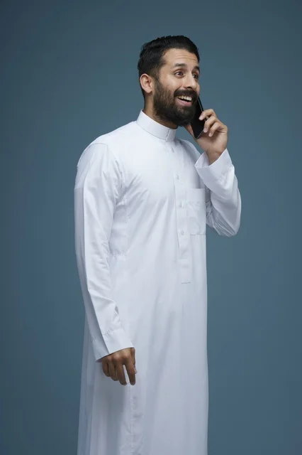 رجل سعودي مبتسم يتحدث عبر الهاتف الذكي بالثوب