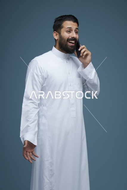 رجل سعودي مبتسم يتحدث بالهاتف الذكي في استوديو