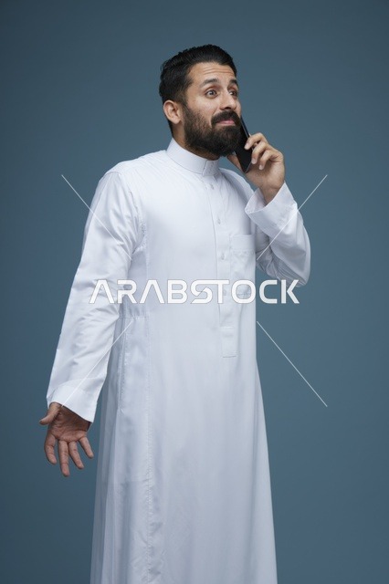 رجل سعودي يتحدث عبر الهاتف الذكي أمام خلفية زرقاء
