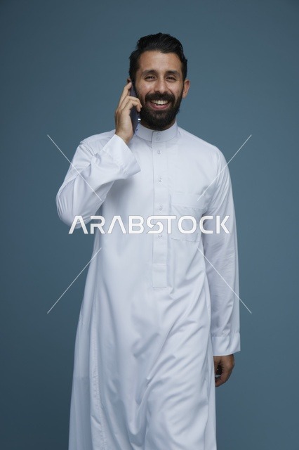 رجل سعودي بالثوب الأبيض يتحدث بالهاتف الذكي