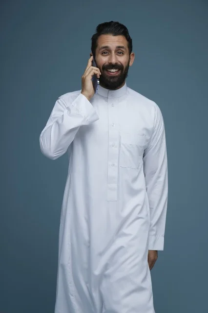 Smiling Saudi Man in White Thobe Talking on Smartphone