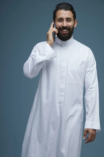 رجل سعودي مبتسم يتحدث عبر الهاتف الذكي بالثوب الأبيض