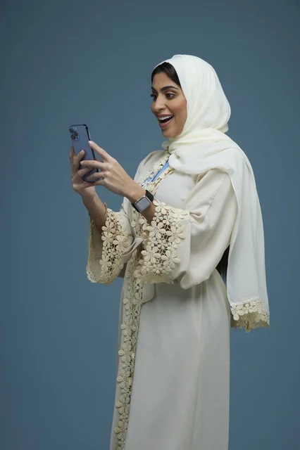 امرأة سعودية تستخدم الهاتف الذكي بعباءة كريمية أنيقة