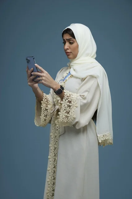 Saudi Woman in Cream Abaya Using Smartphone Blue Background
